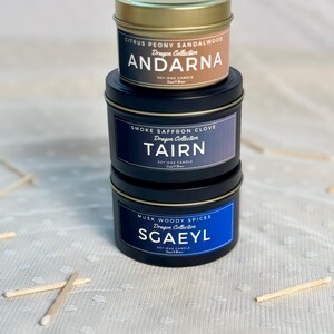 Puede incluir: Tres velas de cera de soja en latas negras con tapas doradas. La vela superior est&aacute; etiquetada como "Citrus Peony Sandalwood Dragon Collection ANDARNA", la vela del medio est&aacute; etiquetada como "Smoke Saffron Clove Dragon Collection TAIRN", y la vela inferior est&aacute; etiquetada como "Musk Woody Spices Dragon Collection SGAEYL".