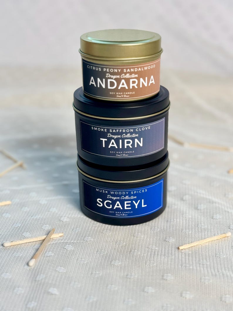 Puede incluir: Tres velas de cera de soja en latas negras con tapas doradas. La vela superior est&aacute; etiquetada como "Citrus Peony Sandalwood Dragon Collection ANDARNA", la vela del medio est&aacute; etiquetada como "Smoke Saffron Clove Dragon Collection TAIRN", y la vela inferior est&aacute; etiquetada como "Musk Woody Spices Dragon Collection SGAEYL".
