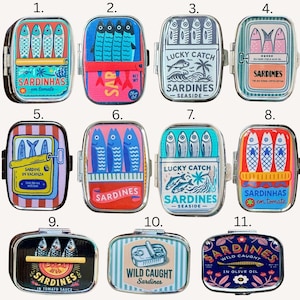 May include: A collection of eleven rectangular metal tins featuring colorful graphic illustrations of sardines. Each tin displays unique artwork with various sardine motifs, text labels like Sardinhas, Lucky Catch, and Wild Caught, and vibrant color palettes including red, blue, yellow, and pink.
