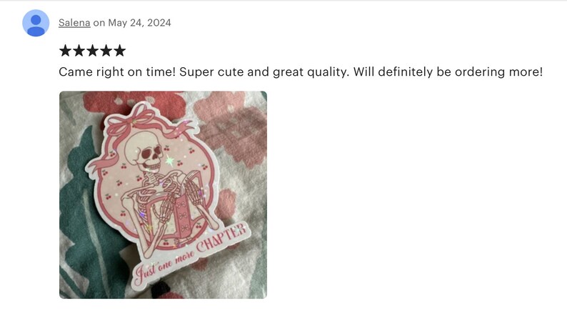 May include: Pink and white sticker with a skeleton holding a book. The sticker has a pink ribbon and the text "Just one more CHAPTER".