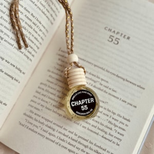 Könnte beinhalten: Ein runder, schwarz-weißer Auto-Lufterfrischer mit einer goldenen Kette. Der Lufterfrischer ist rund und hat ein schwarzes Etikett mit der Aufschrift "Smells Like Pure Smut" und "Chapter 55" mit den Worten "Cauldron Boil Me" darunter.