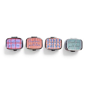 Puede incluir: Cuatro pastilleros rectangulares con ribete plateado. Cada caja tiene una tapa estampada diferente: morada con cuadr&iacute;cula roja, roja con rayas blancas, azul con cuadr&iacute;cula roja y verde con rayas azules. Cada caja tiene el texto "Custom pill box".