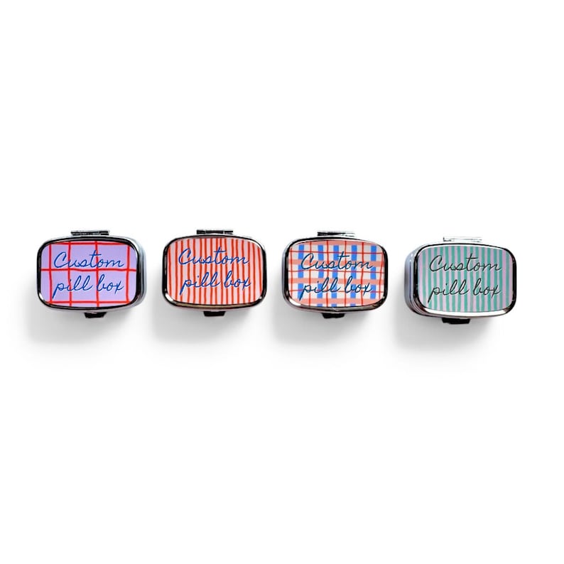 Puede incluir: Cuatro pastilleros rectangulares con ribete plateado. Cada caja tiene una tapa estampada diferente: morada con cuadr&iacute;cula roja, roja con rayas blancas, azul con cuadr&iacute;cula roja y verde con rayas azules. Cada caja tiene el texto "Custom pill box".
