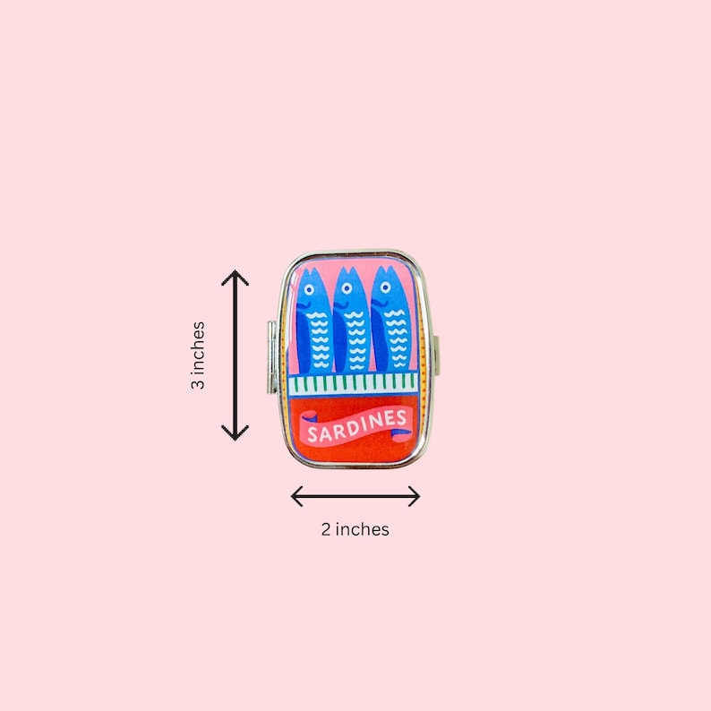 May include: A rectangular metal pill case featuring a colorful graphic of three blue fish on a pink background above a red section with the text SARDINES. The case measures 3 inches in height and 2 inches in width as indicated by the visible arrows.