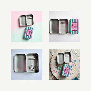 May include: A rectangular metal tin with a hinged lid featuring vertical green and purple stripes and a graphic of sardines with the text SARDINES. The interior contains a magnetic strip holding several sewing needles and a teapot-shaped needle minder.