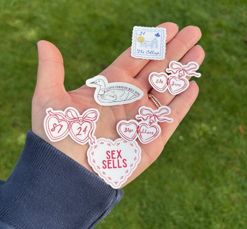 K&ouml;nnte beinhalten: Eine Sammlung wei&szlig;er Aufkleber mit roten Akzenten und Text. Die Aufkleber umfassen ein herzf&ouml;rmiges Design mit den Worten "SEX SELLS", eine Briefmarke mit einer Hausillustration und eine Zeichnung eines Vogels. Andere Aufkleber haben Namen und Zahlen.