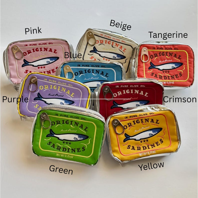 May include: A collection of eight rectangular zippered pouches in pink, beige, tangerine, blue, purple, crimson, green, and yellow. Each pouch features a sardine graphic, the text "ORIGINAL SARDINES" and "IN PURE OLIVE OIL", and a metal pull tab.