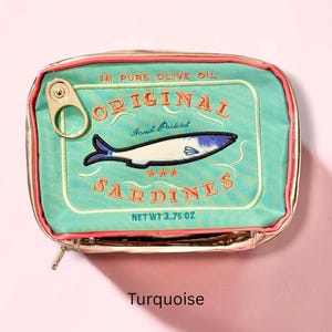 May include: A rectangular turquoise zippered pouch designed to resemble a tin of sardines. The front features embroidered text reading ORIGINAL SARDINES, IN PURE OLIVE OIL, HAND PACKED, and NET WT 3.75 OZ, with a fish graphic and a metal pull tab.