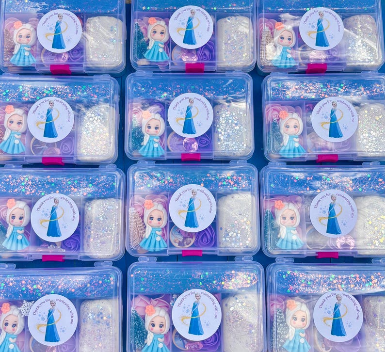 May include: Multiple clear plastic boxes filled with craft supplies. Each box contains a small doll, glitter, and decorative elements. The boxes are decorated with stickers featuring a princess and the text "Thank you for celebrating with me."