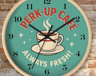 May include: A round wall clock with a light wood frame. The clock face is teal with a coffee cup illustration and the words "PERK-UP CAFE" and "ALWAYS FRESH!". Black hands indicate the time. The clock is against a brick wall.