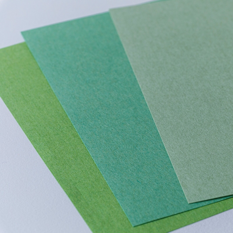 Pode incluir: Tr&ecirc;s folhas de papel em diferentes tons de verde. O papel &eacute; texturizado e tem um brilho sutil.