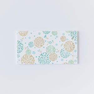 May include: A white notebook with a floral pattern in shades of green and gold. The notebook is bound with a white string.