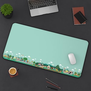 May include: A rectangular desk mat with a solid light teal background and a horizontal border along the bottom edge featuring a colorful, pixelated landscape illustration of trees, mountains, small buildings, and various small animal characters.