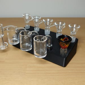 May include: A black stand with a variety of glass smoking bowls and pipes. The stand has a variety of different sized bowls and pipes, including a small bowl with a swirl design.