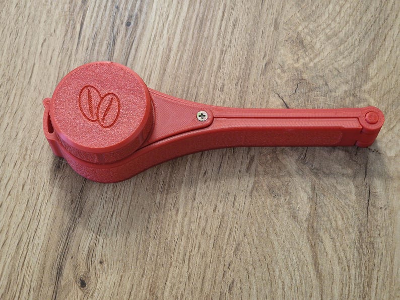 May include: A red plastic coffee scoop with a hinged handle and a round, removable container with a coffee bean logo.
