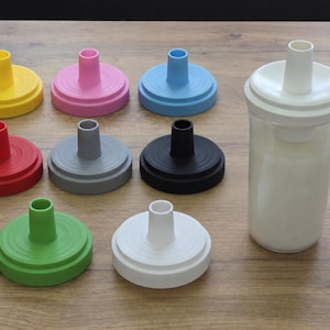 May include: A collection of circular plastic lids with central spouts in yellow, pink, light blue, red, gray, black, green, and white, alongside a clear plastic cup with a white lid and spout, featuring concentric ring details on the top surface.