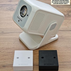 Puede incluir: Un proyector Magcubic blanco con lente plateada y soporte blanco. Dos pequeños soportes cuadrados, uno blanco y otro negro, están debajo. El texto en los soportes dice "3D-WOLFSHOP". La imagen incluye una advertencia: "NO PROJECTOR INCLUDED".