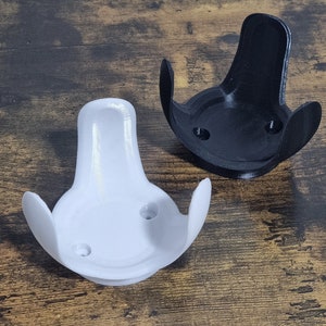May include: Two 3D printed wall mounts, one white and one black, designed to hold a smart speaker or other device. The mounts have a curved shape with three prongs and two small holes on the bottom.