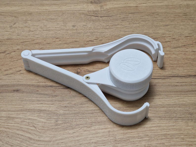 May include: White plastic tool with a hinged design. The tool has a round, white cap with a logo on it. The tool is designed to open and close containers.
