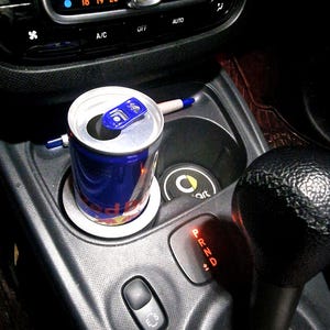 Könnte beinhalten: Eine rote und blaue Energy-Drink-Dose in einem Getränkehalter in einem Auto. Der Schalthebel des Autos ist mit den Buchstaben P, R, N, D und +1 sichtbar.