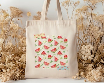 May include: A white canvas tote bag with a watermelon print. The bag has a red, green, and pink watermelon pattern with green leaves. The bag has a light brown handle.