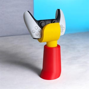 May include: A red, yellow, and white gaming controller stand. The stand is designed to hold a white gaming controller. The base is red, the middle section is yellow, and the controller is white.