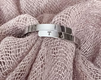 May include: A silver-toned adjustable wrap ring featuring a polished finish and the letter T engraved on the band. The text Minimalist Adjustable Wrap Ring in mirror polished 316L stainless steel or 14K gold plated is visible above the ring.