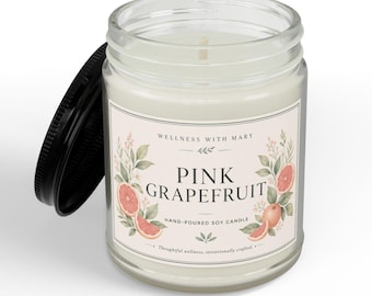 May include: A clear glass jar candle with a black lid, filled with white soy wax. The label features the text Wellness With Mary, Pink Grapefruit, and Hand-Poured Soy Candle, decorated with watercolor illustrations of pink grapefruit slices and green leaves.