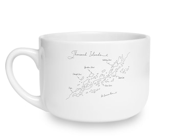 May include: A white ceramic mug featuring a black line drawing of the Thousand Islands region. The design includes a map of the islands with labels for Wellesley Island, Grindstone Island, Clayton, Heart Island, and the St. Lawrence River.