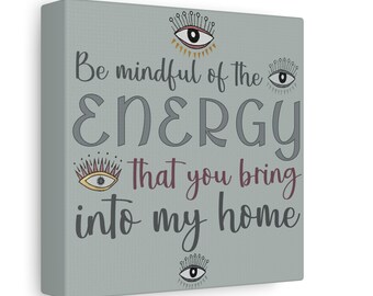May include: A square canvas wall art piece with a sage green background featuring the text "Be mindful of the ENERGY that you bring into my home" in dark gray and maroon lettering, accented by four stylized eye illustrations with lashes.