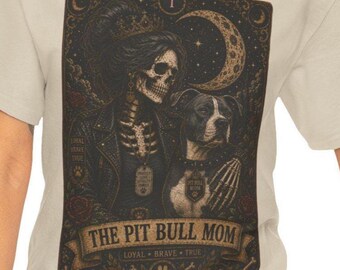 May include: A beige t-shirt featuring a graphic print of a skeleton wearing a crown and leather jacket, standing next to a pit bull dog. The design resembles a tarot card with a crescent moon, roses, and the text THE PIT BULL MOM, LOYAL, BRAVE, TRUE.