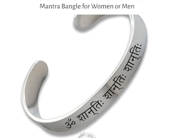 May include: A silver-toned metal cuff bangle featuring the Sanskrit mantra Om Shanti Shanti Shanti engraved in black lettering along the outer surface. The open-ended bracelet has a smooth, polished finish and a curved, minimalist design.