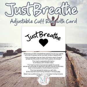 May include: An image featuring a white card with the words "Just Breathe" and a black heart. The card is accompanied by an adjustable cuff ring. The text on the card encourages mindfulness and self-care.
