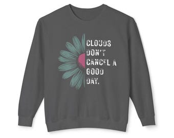 May include: Dark gray sweatshirt with a daisy graphic. The daisy is half teal and half pink, with the text "CLOUDS DON'T CANCEL A GOOD DAY." The sweatshirt has long sleeves and a crew neck.