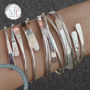 May include: A set of silver and copper bangle bracelets with a hammered finish. The bracelets are stacked on a person's wrist. Purchase as a set or separately.