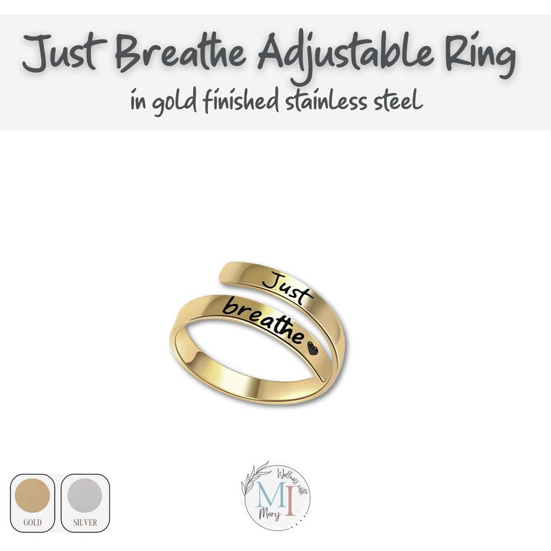 May include: Gold-finished stainless steel adjustable ring. The ring is engraved with the words "Just breathe" in black script. The ring has a heart symbol after the word "breathe". The text "Just Breathe Adjustable Ring" is at the top.