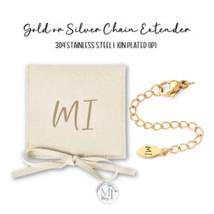 May include: A gold chain extender with a lobster clasp and a small tag with "MI" engraved. The extender is next to a beige pouch with "MI" printed on it. The text "Gold or Silver Chain Extender" is at the top.