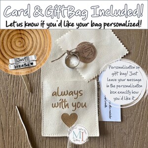 May include: A gift set featuring a silver ring, a small bag with "always with you" and a heart, and a wooden coaster with "Just breathe" engraved on a ring. The set includes a gift bag and card.