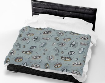 May include: A light blue duvet cover featuring a repeating pattern of stylized eyes in various shapes and sizes. The eyes are outlined in black with accents of white, gold, and dark red, and are arranged across the fabric surface.