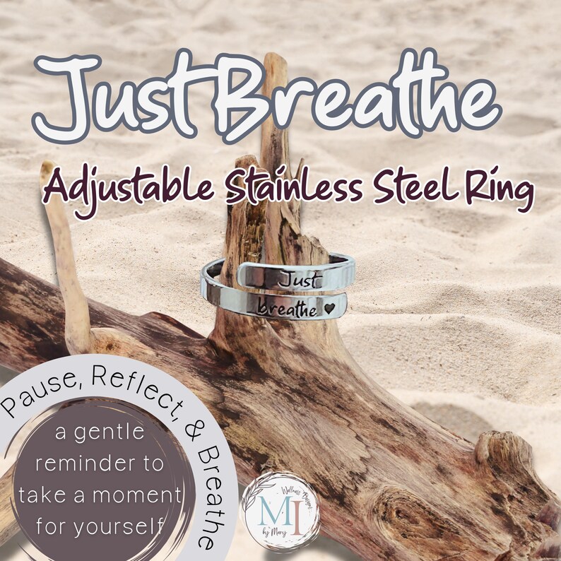 May include: An adjustable stainless steel ring with the words "Just Breathe" engraved on it. The ring is silver and sits on a piece of driftwood. The image also includes the text "Pause, Reflect, & Breathe."