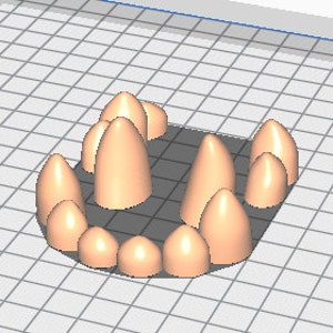 May include: A set of 14 sharp, pointed teeth made of a light brown material. The teeth are arranged in a curved shape, resembling a mouth.