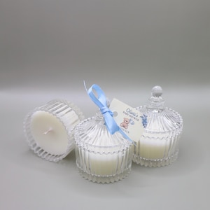 May include: Three clear glass candle jars with white candles. The center jar has a blue ribbon and a tag that reads "Olivia's Baby Shower Thank You".