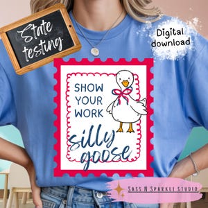 May include: Light blue t-shirt featuring a whimsical design with a cartoon goose and the phrase "Show Your Work Silly Goose" in a red and white frame. A small chalkboard with the words "State testing" is in the upper left corner. "Digital download" is written on the upper right.