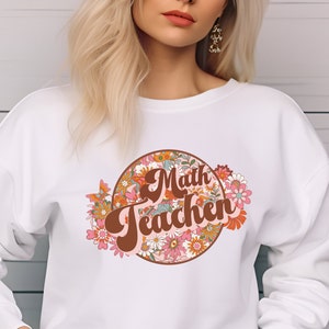 May include: White sweatshirt with a brown and pink floral design and the text "Math Teacher" in a retro font.