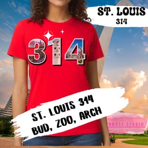 May include: A red t-shirt featuring the text "ST. LOUIS 314 BUD, ZOO, ARCH". The number "314" is designed with images of local landmarks. The shirt has a crew neck and short sleeves.