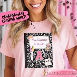 May include: A pink teacher t-shirt with a black and white notebook design. The notebook has a rainbow, a coffee cup, a pencil, a highlighter, and the text "Mrs. Anderson 1st Grade".