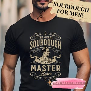May include: A black t-shirt with a vintage-style graphic design featuring a man with a mustache and the text "The Great Sourdough - Stretch & Fold - Master Baker".