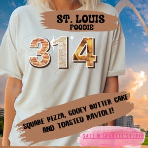 May include: Cream-colored t-shirt with the text "ST. LOUIS FOODIE" and the number "314" in a pizza-like font. Below, it reads "SQUARE PIZZA, GOOEY BUTTER CAKE AND TOASTED RAVIOLI!" in a brown banner.