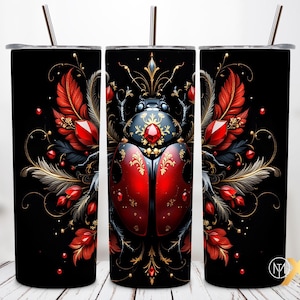 Pode incluir: Caneca preta com uma ilustração detalhada de um besouro com tons de joia. O besouro é vermelho e preto com detalhes dourados e uma grande gema vermelha. O design inclui penas vermelhas, pedras preciosas e detalhes dourados. A caneca tem um canudo prateado.