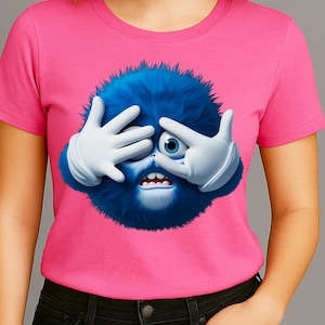 May include: A pink crew neck t-shirt featuring a cartoon character. The character is a blue, furry creature with white gloved hands covering its eyes. The creature has one eye visible and an open mouth.